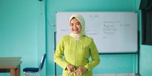 A smiling woman stands in front of a whiteboard.